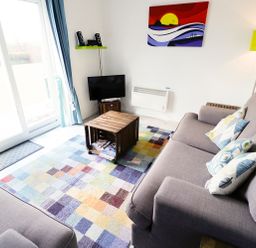 A living room with two gray sofas a colorful checkered rug a wooden crate coffee table a small TV and speakers on a green shelf at Driftwood in Bude