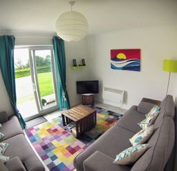 A living room with two grey sofas a colorful rug a small wooden coffee table and a television at Driftwood in Bude