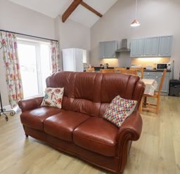 A living room with a brown sofa and kitchen area at Coetsiws in Clynnog Fawr