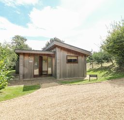 A wooden house with a gravel driveway and surrounding trees at Tickencote in Exton Rutland