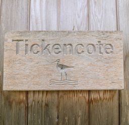 A wooden sign with the word Tickencote and a bird design mounted on a wooden surface at Tickencote Exton Rutland