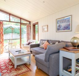 A living room with a gray sofa white armchair wooden coffee table and glass doors leading to a patio at Tickencote in Exton Rutland