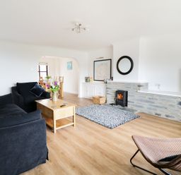 A living room with a black sofa armchair wooden coffee table stone fireplace and dining area at Seal Cottage in Mortehoe