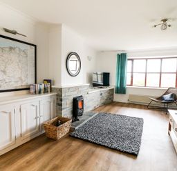 A living room with a fireplace television chair and a large window with blue curtains at Seal Cottage in Mortehoe