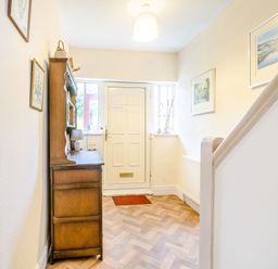 A hallway with a wooden cabinet a white door framed pictures and a staircase at The Perks in Scarborough