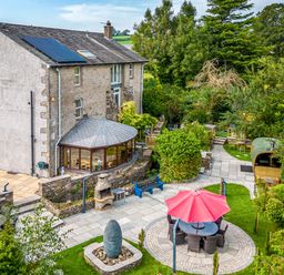 An outdoor garden area with patio furniture and a red umbrella next to a stone house at Eden Mill Millers Beck in Kendal