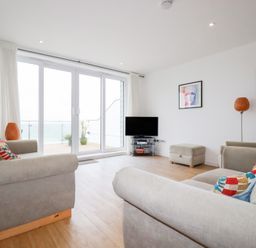A living room with gray sofas a television on a stand and large glass doors leading to a balcony at Buena Vista in Newquay
