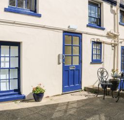 A courtyard with blue doors and windows a table with two chairs and potted plants at The Compass in Swanage