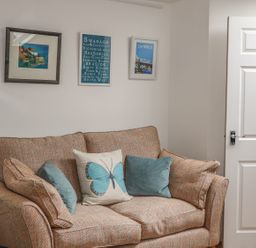 A sofa with cushions and framed pictures on a wall next to a white door at The Compass in Swanage