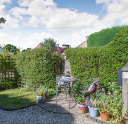 A small garden with a table and two chairs surrounded by potted plants and hedges at Puffitts Cottage in Bourton-on-the-Water