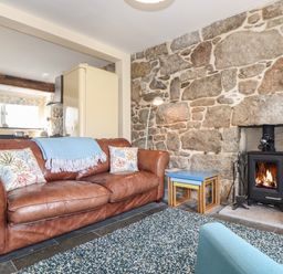 A living room with a leather sofa and a wood burning stove in a stone wall at Mermaid Cottage in Mousehole