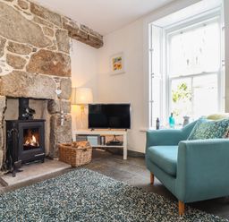 A living room with a stone fireplace a blue armchair and a television at Mermaid Cottage in Mousehole