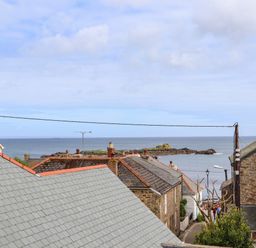 Rooftops of stone houses with chimneys and a view of the sea and rocky coast at Mermaid Cottage in Mousehole