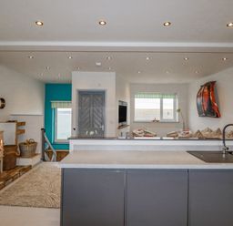 An open living space with a kitchen island a wood stove and a seating area with windows showing an ocean view at Sailor's Rest in Newquay