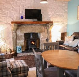 A living room with a stone fireplace and wood-burning stove a wooden dining table with chairs a plaid armchair and a leather sofa with cushions at Mary Larkin's Cottage Rostrevor near Newry