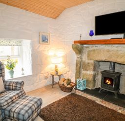 A room with a fireplace and a black wood stove a plaid armchair with an ottoman and a small side table with a lamp at Mary Larkin's Cottage Rostrevor near Newry