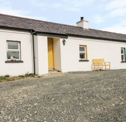 A white cottage with a yellow door and bench a gravel area in front at Mary Larkin's Cottage in Rostrevor near Newry