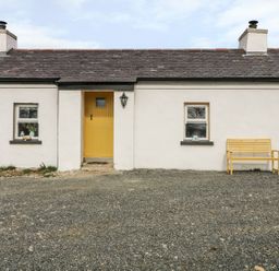A one-story cottage with a yellow door two windows and a yellow bench outside at Mary Larkin's Cottage Rostrevor near Newry