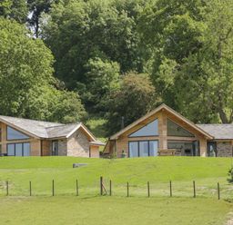 Two wooden and stone houses on a grassy hill with trees in the background at Shepherd's Rest in Montgomery