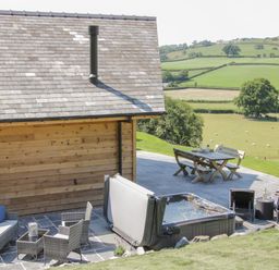 An outdoor patio with a hot tub seating area and dining table overlooking green fields at Shepherd's Rest in Montgomery