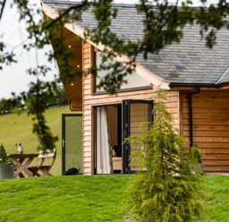 An exterior view of a wooden house with open glass doors and outdoor wooden table and chairs on green grass at Shepherd's Rest in Montgomery