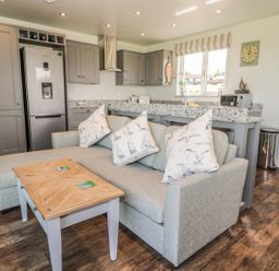 A kitchen with grey cabinets and a silver refrigerator next to a grey sofa with printed cushions and a wooden coffee table at Emblestones in Embleton