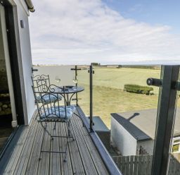 A balcony with a metal table and two chairs overlooking fields and a distant sea at Emblestones in Embleton