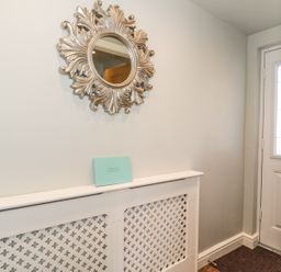A hallway with a decorative mirror above a radiator cover and a white door at Emblestones in Embleton