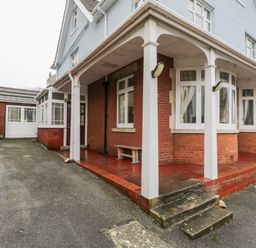 The exterior of a house with a covered porch supported by white columns and a driveway leading to a garage at 20 Ulwell Road in Swanage