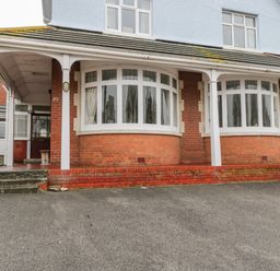 The front view of a two-story house with a tiled roof two large bay windows and a covered porch area at 20 Ulwell Road in Swanage