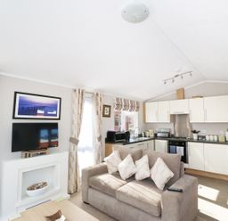 A living room with a sofa TV and kitchen area with cabinets at 32 Cruachan Lodge in Auchterarder