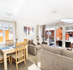 A dining area with a wooden table and chairs next to a living room with sofas and large windows at 32 Cruachan Lodge in Auchterarder