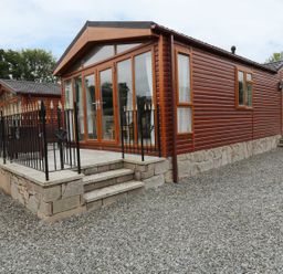 A brown wooden lodge with a stone base and small steps leading to a fenced patio at 32 Cruachan Lodge in Auchterarder