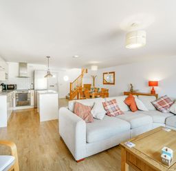 An open-plan living area with a beige sectional sofa and wooden coffee table next to a kitchen with white cabinets and stainless appliances at Coney Garth Barn in Beckermet