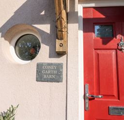 A red front door with a nameplate at Coney Garth Barn in Beckermet