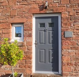 A door and window on a brick wall with a plant at Coney Garth Cottage in Beckermet
