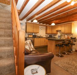 A living area with a staircase a kitchen island with bar stools and leather sofas at Bwthyn Ael Y Bryn in Criccieth