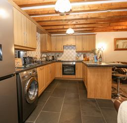 A kitchen with wooden cabinets black appliances and a seating area at Bwthyn Ael Y Bryn in Criccieth