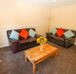 A living room with two brown leather sofas a wooden coffee table with sunflowers and cushions at Howards Hill West in Cromer