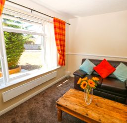 A living room with a brown leather sofa with three cushions and a wooden coffee table with sunflowers in a vase at Howards Hill West in Cromer