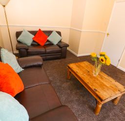 A living room with brown leather sofas cushions on a wooden coffee table and flowers at Howards Hill West in Cromer