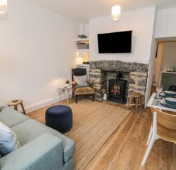 A living room with a sofa, armchair, ottoman, rug, fireplace, TV, and a small dining table set at Llys Madoc in Porthmadog