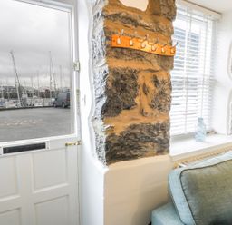 A corner of a room with a door open to a marina outside a stone wall with hooks a window and a blue sofa at Llys Madoc in Porthmadog