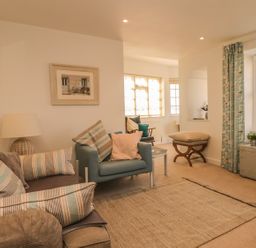 A living room with a sofa and armchair with striped pillows a lamp a framed picture on the wall a window with curtains and a chest at Searles in Lympstone