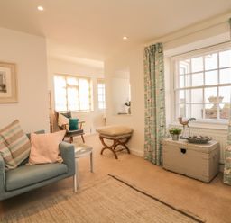 A sitting room with armchair cushions a wooden chair window curtains and a chest at Searles in Lympstone