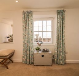A room with a window with turquoise curtains a wooden bench with cushions and a painted chest with decorations at Searles in Lympstone