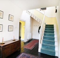 A hallway with a green carpeted staircase wooden chest of drawers and framed pictures on the wall at Glebe House in Wells