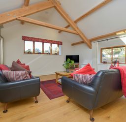 A living room with two black leather sofas and wooden beams at Old Armoury Barn Ashburton