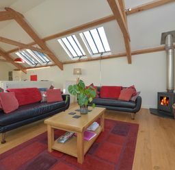 A living room with two black sofas red cushions a wooden coffee table a fireplace and skylights at Old Armoury Barn Ashburton