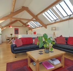 A living room with black sofas and red cushions under skylights with wooden beams at Old Armoury Barn in Ashburton